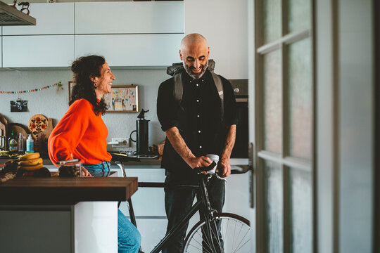Smiling woman talking to man standing with bicycle at home