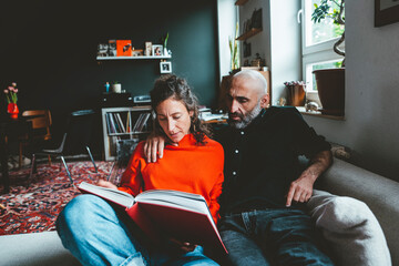 Woman sharing book with man sitting on sofa at home