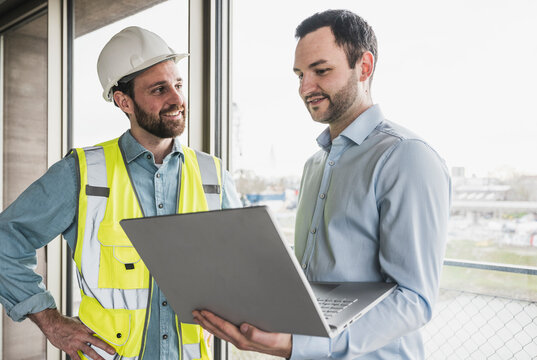 Smiling building contractor looking at architect holding laptop