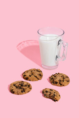 Chocolate chip cookies and glass of milk on pink background