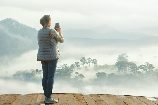 Woman photographs on smartphone beautiful mountain range in foggy clouds in early summer morning.
