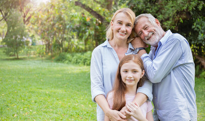 Fototapeta premium Portrait of happy family senior man woman and little girl relax in park. Mature elder family of three having fun together outdoor. Home school education, adopted child family lifestyle spring summer