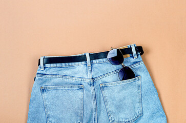 Blue jeans, beige suede loafer or flat shoes lying and sunglasses on beige background.