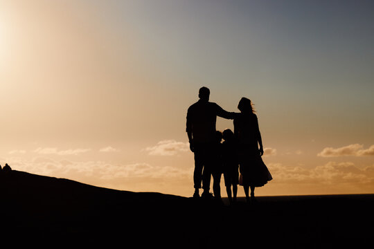 Parents, kids and silhouette on mountain, sunset and hug with love, care and summer adventure. Mother, father and young children with sky background, space and outdoor on holiday, vacation or journey