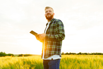 Portrait of a happy farmer. A man with a beard in a shirt and jeans with a tablet. Wheat harvest, eco products