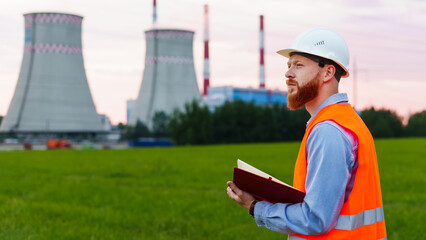 An engineer with a notebook on the background of a power plant. The man is wearing a white helmet...