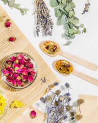 Home herbal apothecary concept. Dry flowers and herbs, tea bags and wooden spoons on wooden napkin on white background. Healing tea from wild plants and flowers.Flat lay, vertical format