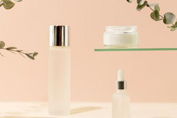 Cosmetic glass jars with natural cream, face serum and organic tonic on pink background with eucalyptus sprigs. Organic beauty product and skin friendly cosmetics concept. Mockup, front view