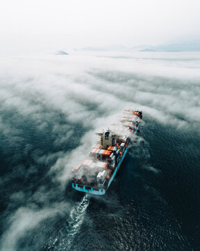 Aerial view of a cargo ship sailing the Hong Kong bay with low clouds, China.