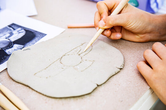 Close-up of child hands in process of making clay sculpture of winged sun disc archeology at workshop