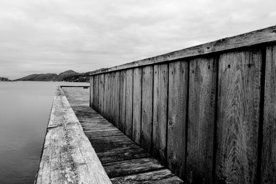 Black And White Monochrome Image Wooden Dock Board Walk Structure At Waters Edge