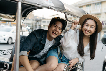 Happy and joyful Young Asian couple traveler tourists riding a tuk tuk tour, rickshaw style transportation on the street in Bangkok in Thailand - people traveling enjoying local culture concept - 607710979