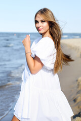 Fototapeta na wymiar Happy, beautiful woman on the ocean beach standing in a white summer dress.
