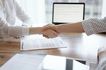 Business people shaking hands above contract papers just signed on the wooden table, close up. Lawyers at meeting. Teamwork, partnership, success concept.