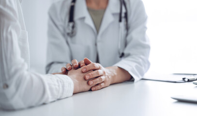 Doctor and patient sitting at the desk in clinic office. The focus is on female physician's hands reassuring woman, close up. Perfect medical service, empathy, and medicine concept.
