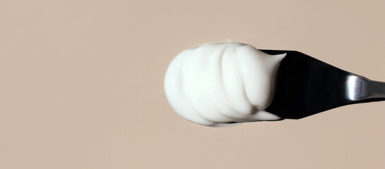 texture of cosmetic cream on a palette knife on a beige background with space for text