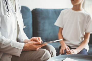 Doctor woman and kid boy patient at home. The pediatrician using tablet computer while filling up medical records, close up. Medicine, healthcare concepts.