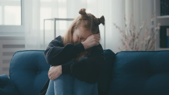 Teenage girl crying bitterly on couch, feeling depressed, adolescence, puberty