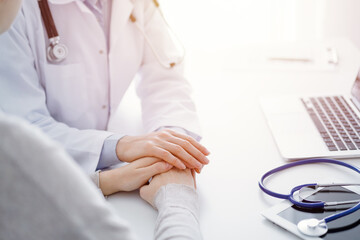 Doctor and patient sitting at the table in clinic office. The focus is on female physician's hands reassuring woman, only hands close up. Medicine concept.