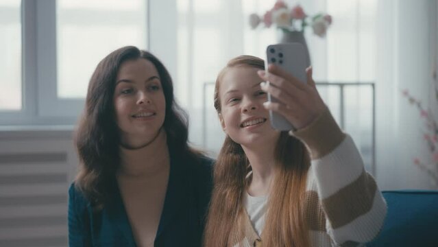 Happy mother and teenage daughter taking selfie on cellphone at home, having fun