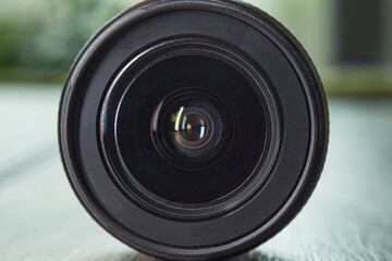 Front view of a DSLR lens. Close-up of the 18-55mm zoom lens lying on a dark wooden background.