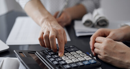 Woman accountant using a calculator and laptop computer while counting taxes for a client. Business audit and finance concepts.