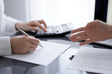 Woman accountant using a calculator and laptop computer while counting and discussing taxes with a client. Business audit concepts.
