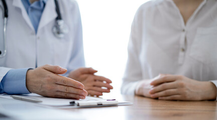 Doctor and patient discussing something while sitting near each other at the wooden desk in clinic, close up of hands. Medicine concept.
