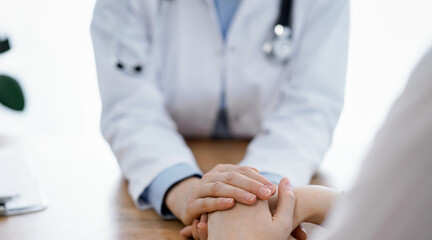 Obraz premium Doctor and patient sitting at the wooden table in clinic. Female physician's hands reassuring woman. Medicine concept.
