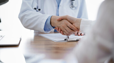 Doctor and patient shaking hands above the wooden table in clinic. Medicine concept.