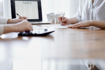 Two accountants using a laptop computer and calculator while counting taxes at wooden desk in office. Teamwork in business audit and finance.