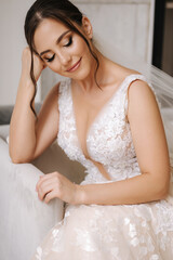Fototapeta na wymiar Attractive young bride sitting on chair in front of big window in her luxury house. Bride morning concept. Wedding day.