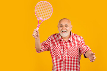 positive old aged man with badminton raquet on yellow background