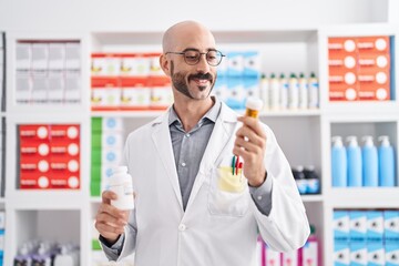 Young hispanic man pharmacist holding pills bottles at pharmacy