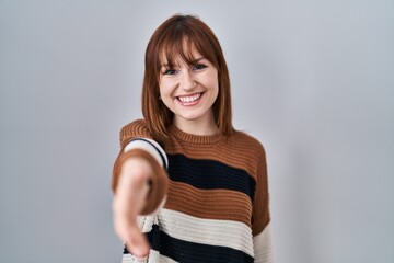 Young beautiful woman wearing striped sweater over isolated background smiling friendly offering handshake as greeting and welcoming. successful business.