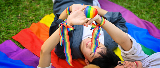 Young people lying on green grass with LGBTQ pride flag, supporting LGBTQ community and equality social