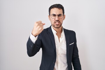 Handsome business hispanic man standing over white background angry and mad raising fist frustrated and furious while shouting with anger. rage and aggressive concept.