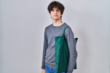 Young man wearing reusable bag thinking attitude and sober expression looking self confident