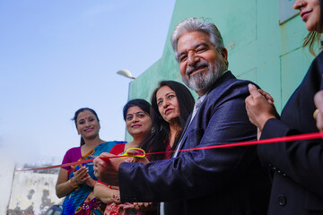Senior businessman cutting red ribbon with women employee group. inauguration concept.