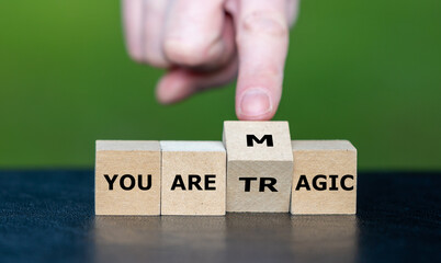 Hand turns wooden cube and changes the expression ' you are tragic' to 'you are magic'.