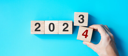 hand holding wooden cube block with 2024 text on blue background. Resolution, plan, review, goal,...