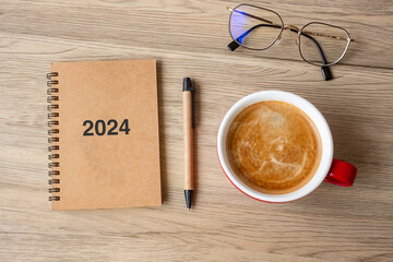 2024 notebook and coffee cup on wood table, Top view and copy space. Xmas, Happy New Year, Goals,...