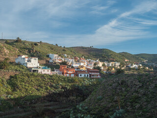 Fototapeta na wymiar Early morning view of village Arure in green valley with palm trees and traditional colorful houses. Valle Gran Rey, La Gomera, Canary Islands, Spain, Europe. Blue sky white clouds background