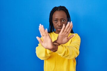 Beautiful black woman standing over blue background rejection expression crossing arms and palms doing negative sign, angry face