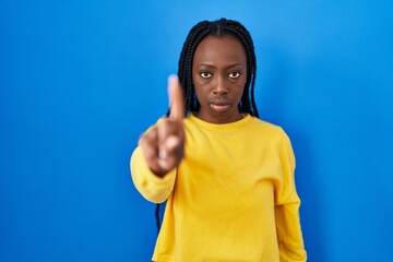 Fototapeta premium Beautiful black woman standing over blue background pointing with finger up and angry expression, showing no gesture