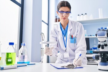 Young beautiful hispanic woman scientist writing report working at laboratory