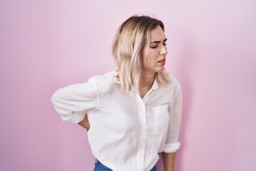 Young beautiful woman standing over pink background suffering of backache, touching back with hand, muscular pain