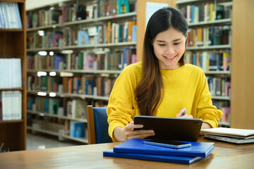 Smiling female college students preparing for exam, searching information on digital tablet in library