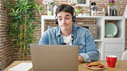 Young hispanic man having online lesson taking notes at dinning room