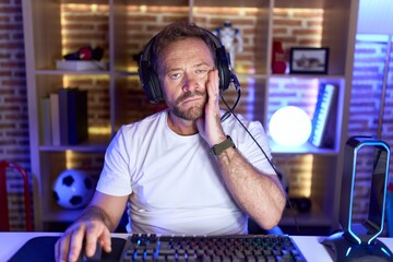 Middle age man with beard playing video games wearing headphones thinking looking tired and bored with depression problems with crossed arms. © Krakenimages.com